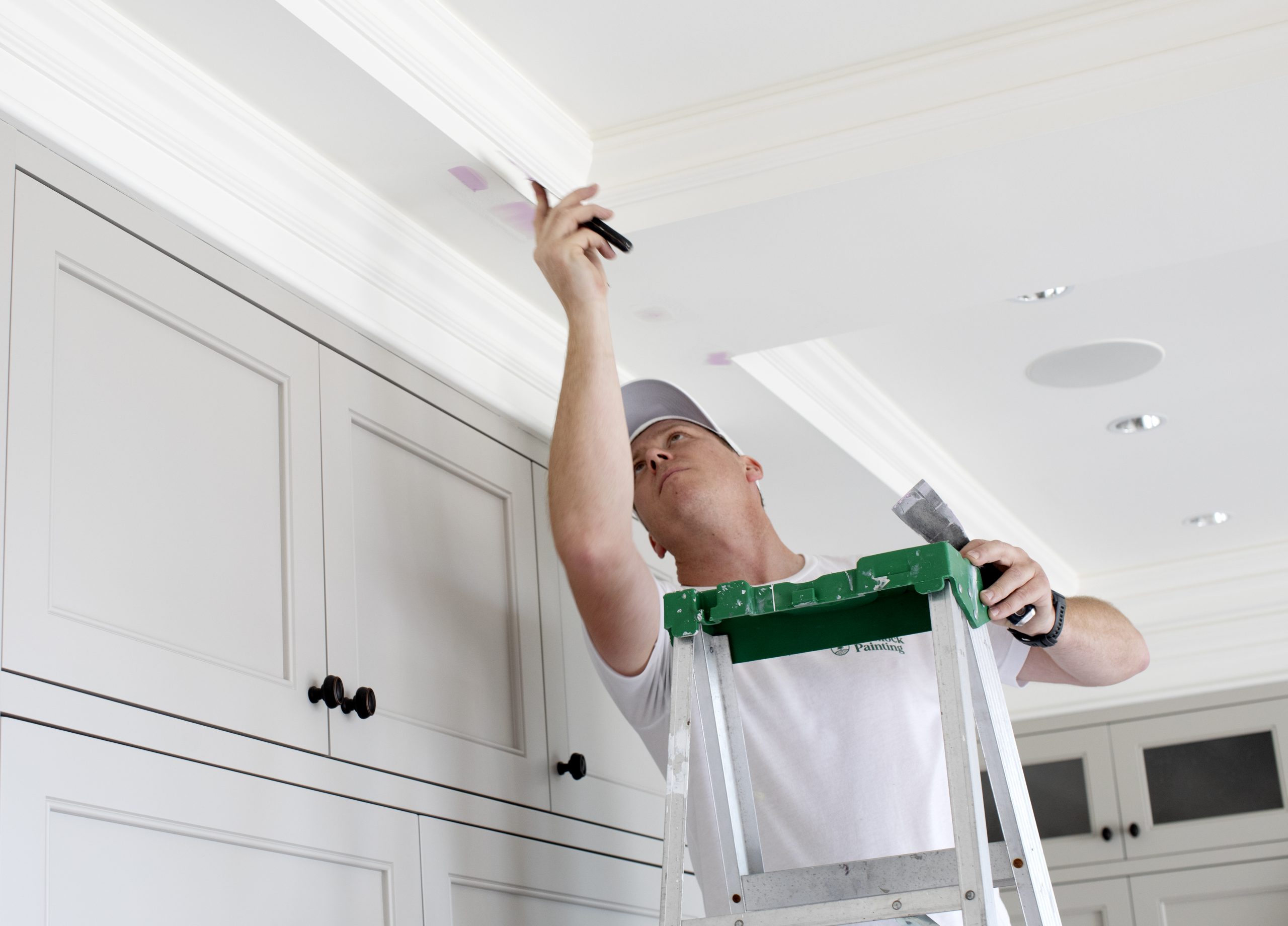 A man dressed in all white stands on a ladder while applying putty to a ceiling
