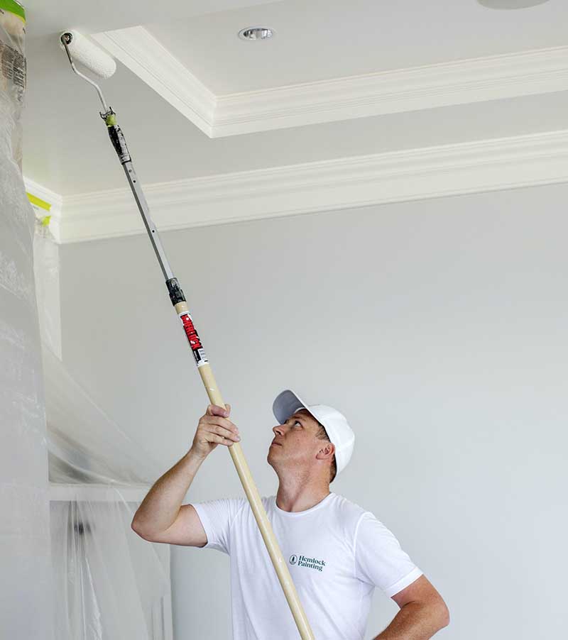 A painter at Hemlock efficiently conducts a high-quality ceiling painting job in an upscale home.